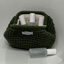 An olive green textured hand woven cosmetic pouch with a white fabric lining, containing several white and frosted bottles, with one matching bottle placed in front on a white surface. A white label on the front of the pouch reads 'VIBES*GRACE'.

