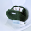 An olive-green crocheted cosmetic pouch filled with glass bottles, with a glass bottle placed in front on a glossy white surface. The VIBES*GRACE brand label is visible on both the pouch tag and the bottle.
