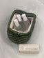 Green woven bag with bottles and a box labeled 'VIBES OF GRACE' on a white surface.


