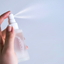 Hand holding a white spray bottle labeled 'Lily Grace' against a light blue background